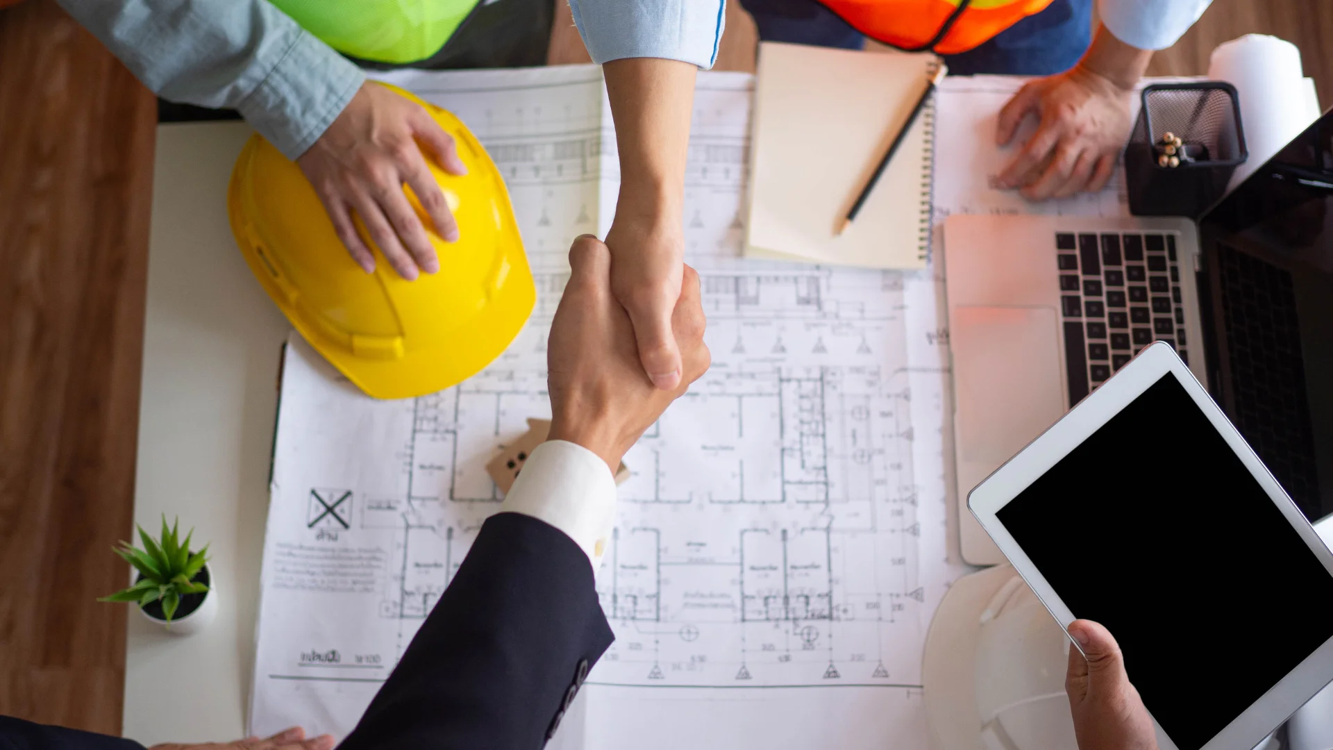 Deux personnes qui se serrent la main devant un plan de construction ce qui permet d'illustrer le métier d'apporteur d'affaires pour architecte